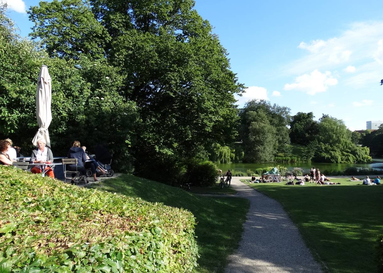 Eine Café-Terrasse und Menschngruppen auf einer Wiese im Park