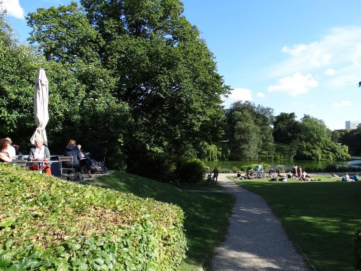 Eine Café-Terrasse und Menschngruppen auf einer Wiese im Park
