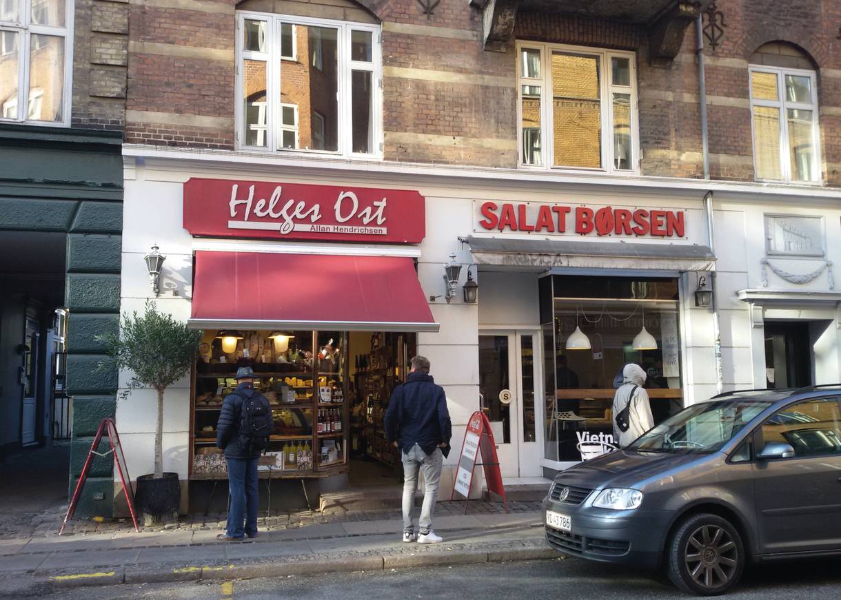 Zwei kleine Lebensmittelgeschäfte mit rotem Schriftzug, davor Kunden