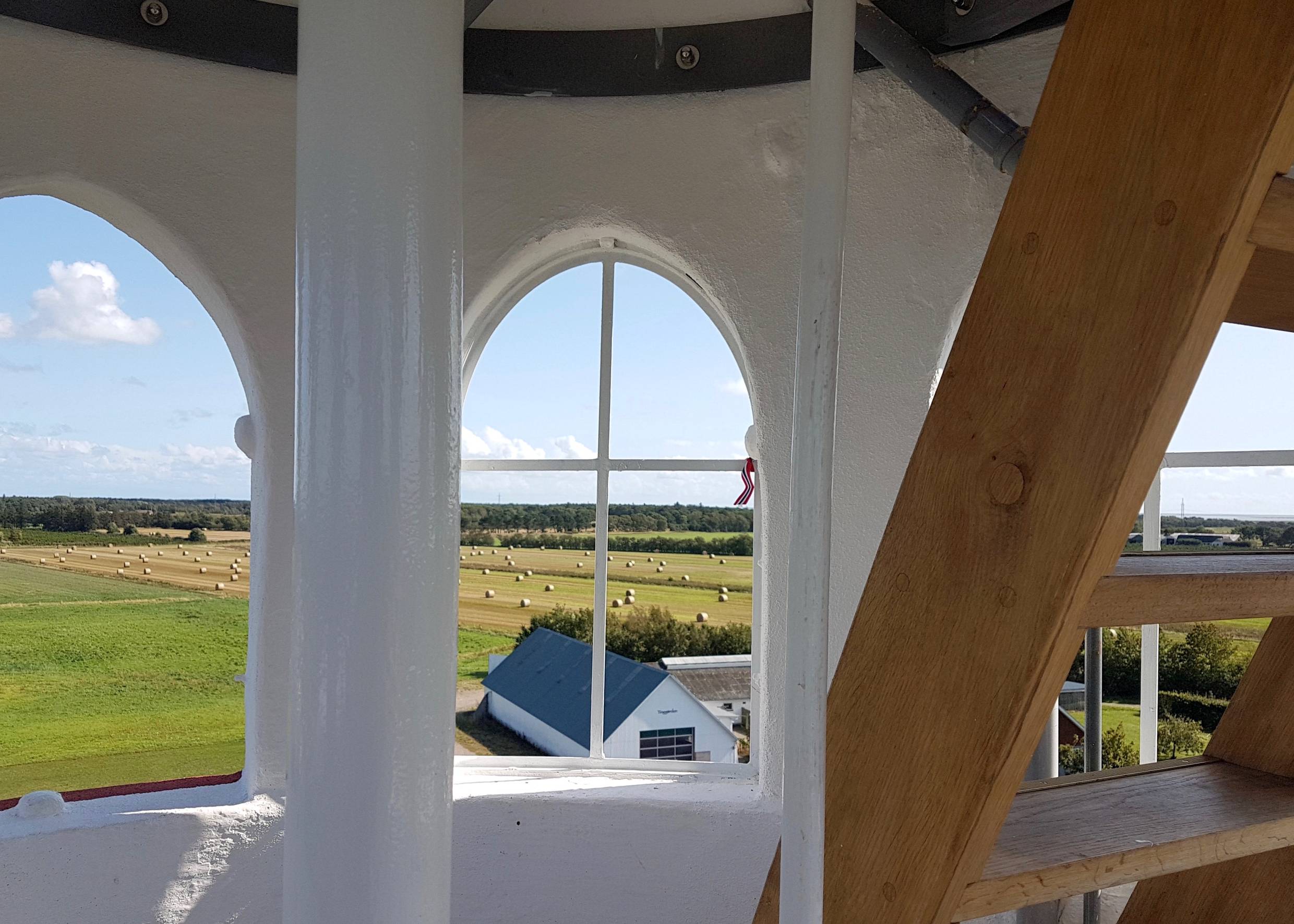 Blick durch bogenförmige Fenster über Stoppelfelder und Wald