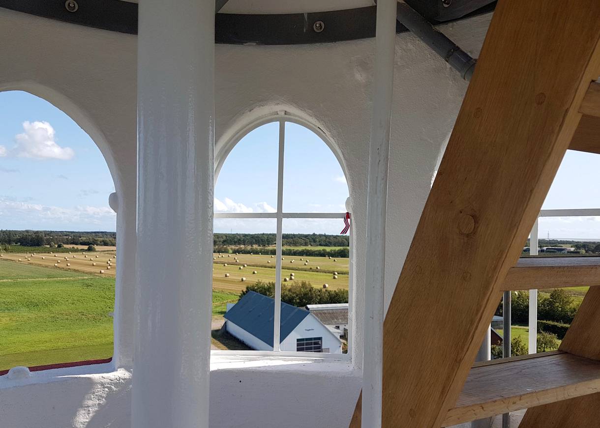 Blick durch bogenförmige Fenster über Stoppelfelder und Wald