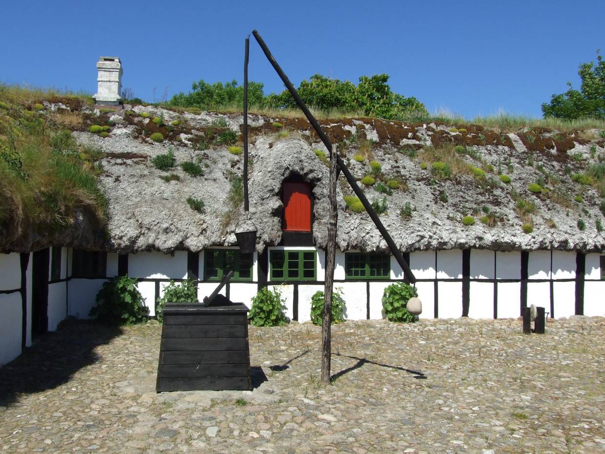 Innenhof des Læsø Museum, ein flaches weißes Bauernhaus mit einem Dach aus Seegras, davor ein schwarzer Ziehbrunnen