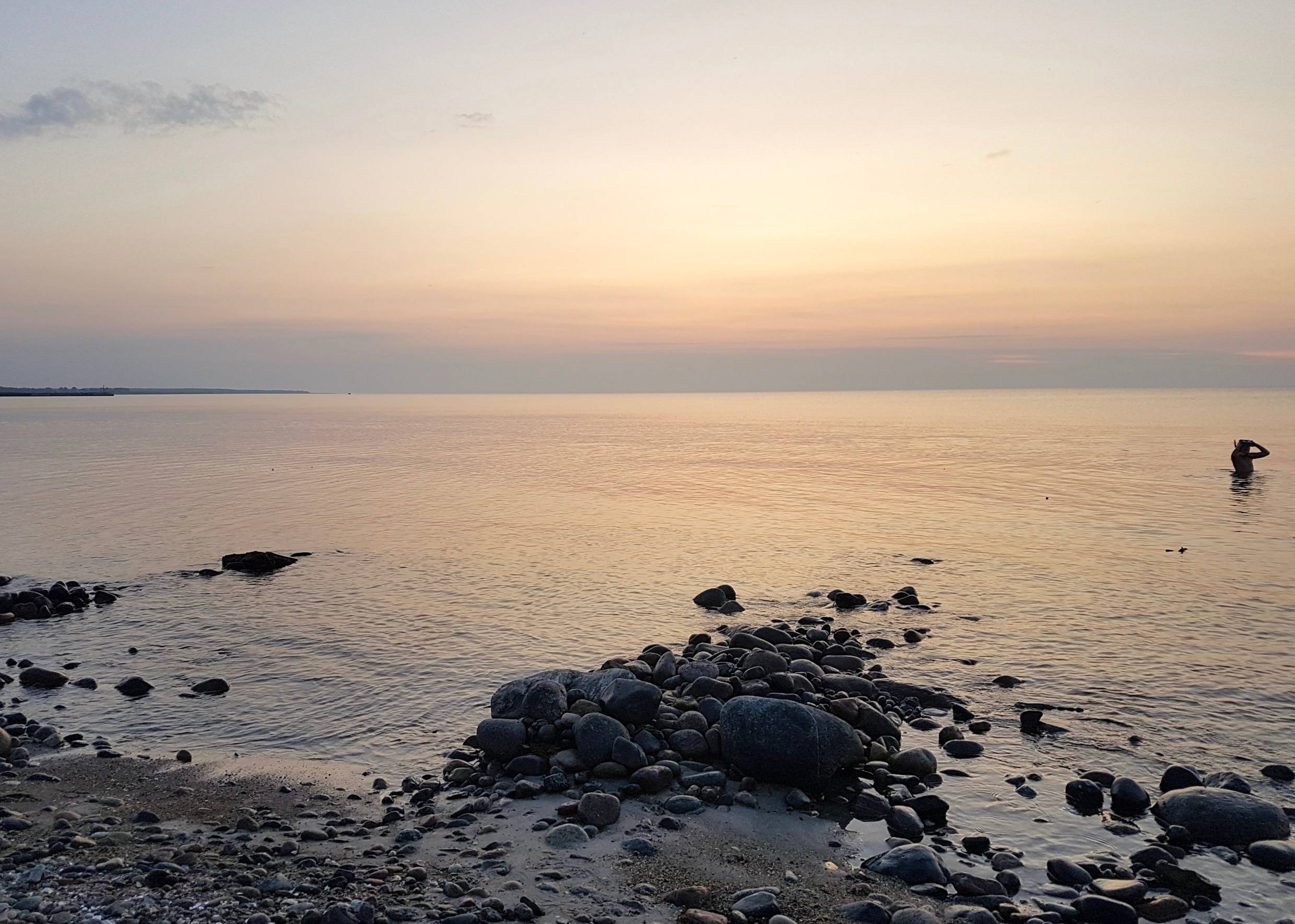 Ostsee mit steinigem Strand in der Abenddämmerung, im Wasser ein Mann