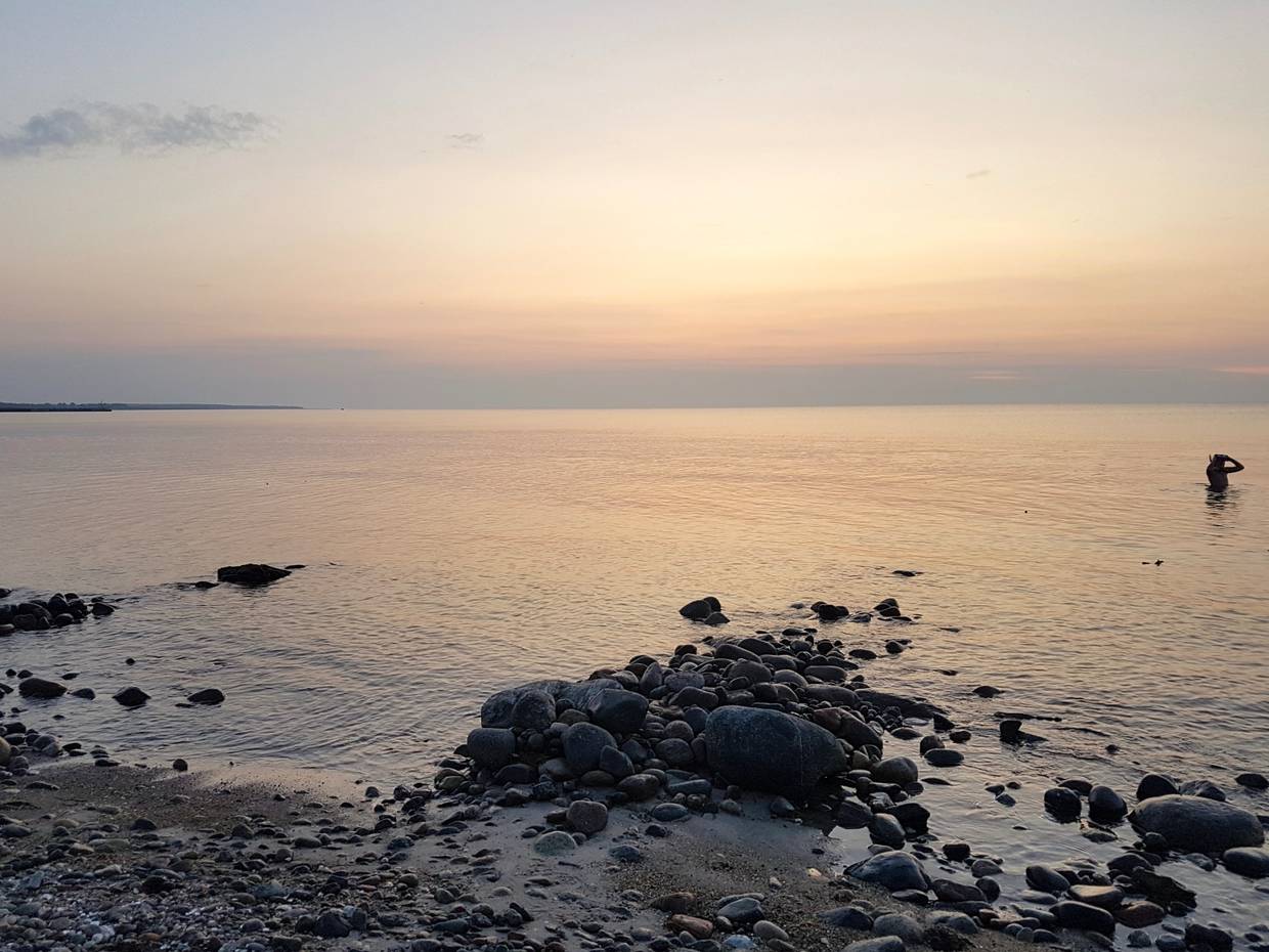 Ostsee mit steinigem Strand in der Abenddämmerung, im Wasser ein Mann