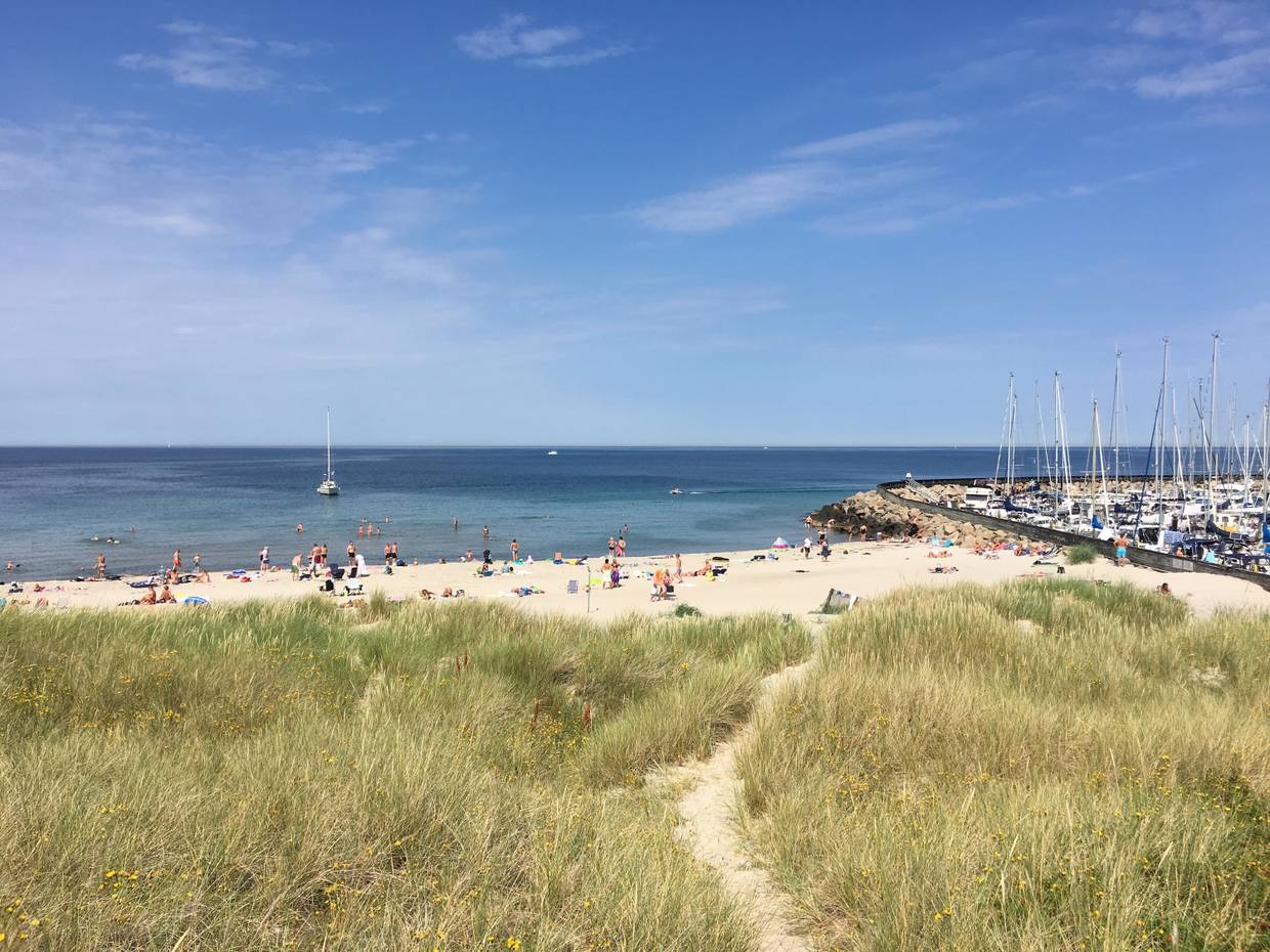 Sandstrand mit Badegäste, nebenan ein Jachthafen