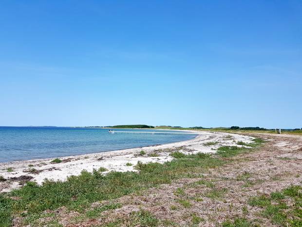 Eine weite Bucht mit einem Badesteg, im Hintergrund eine grüne Landschaft