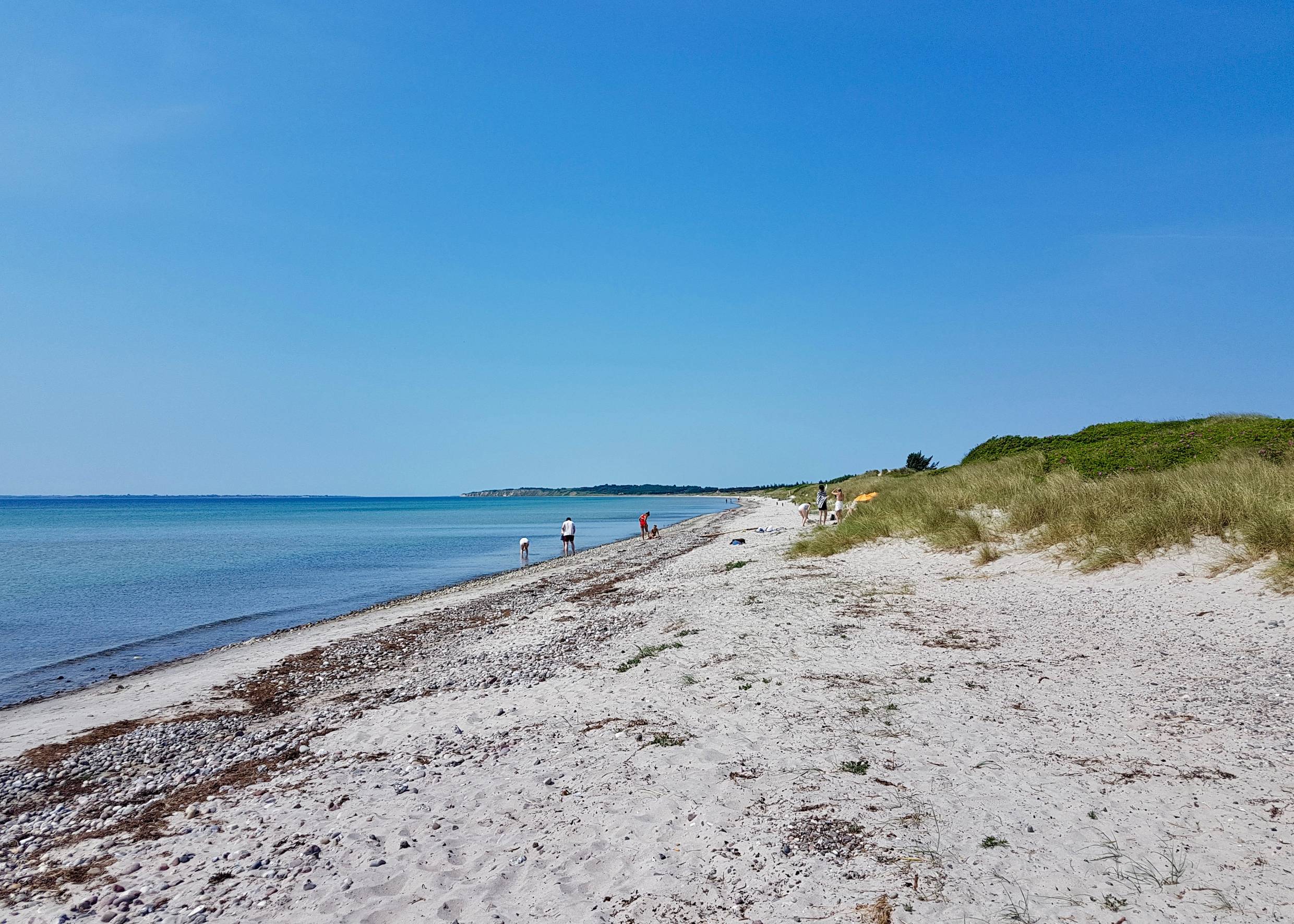 Blick über einen langen Sandstrand mit Steine und Spaziergängern