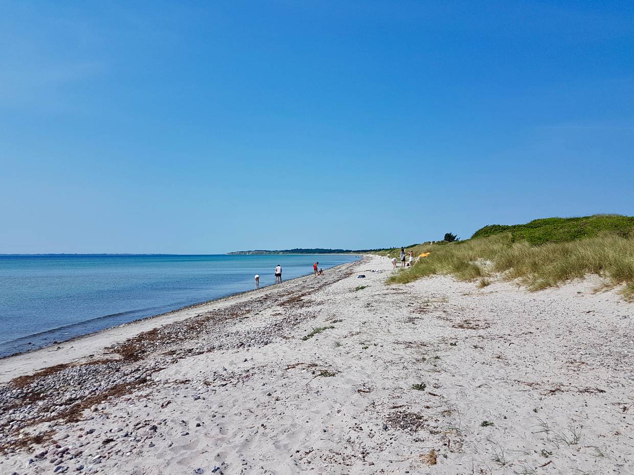 Blick über einen langen Sandstrand mit Steine und Spaziergängern