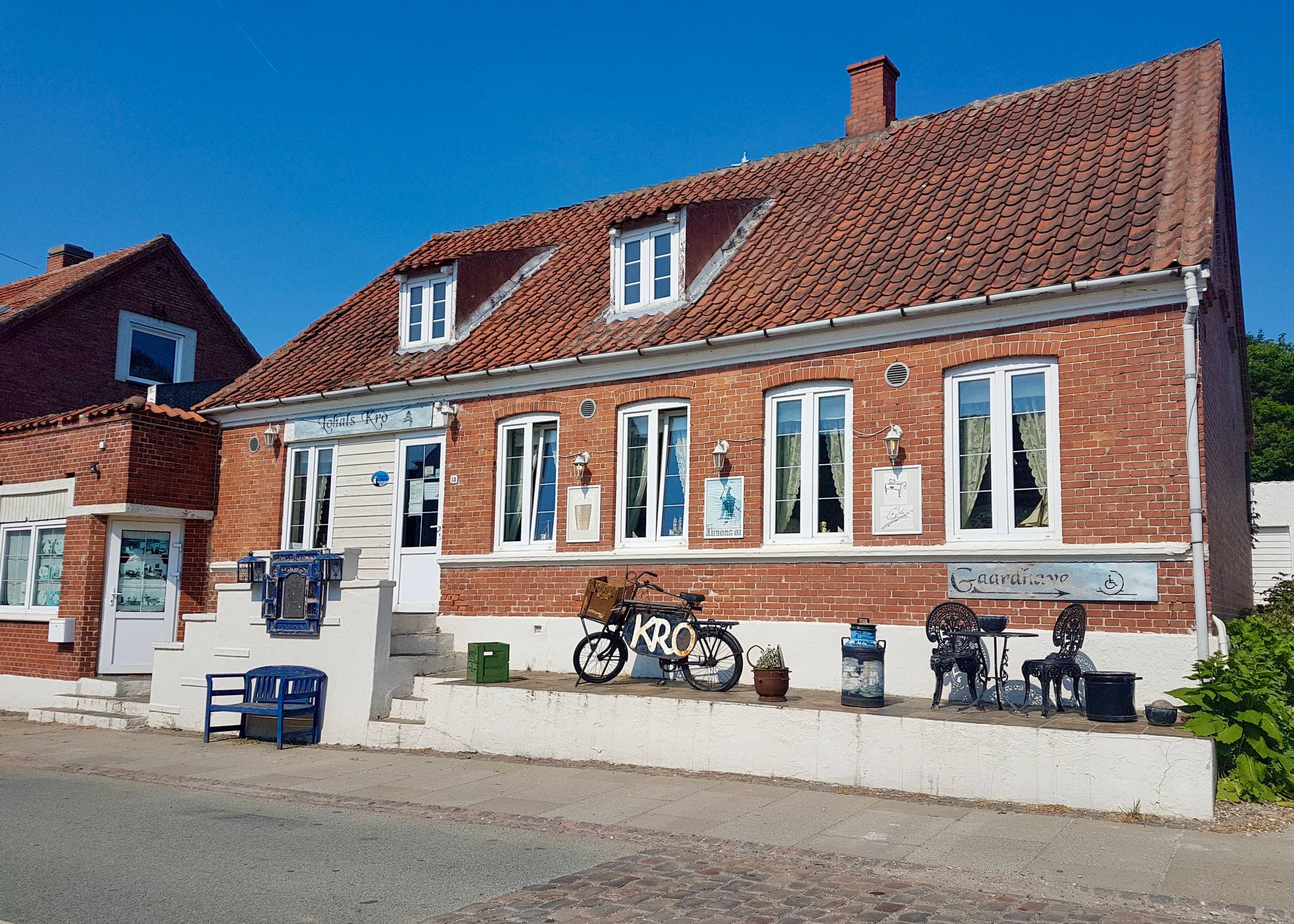 Rotes Backsteinhaus mit einem Lokal, vor der Tür ein altes Fahrrad und Sitzplätze