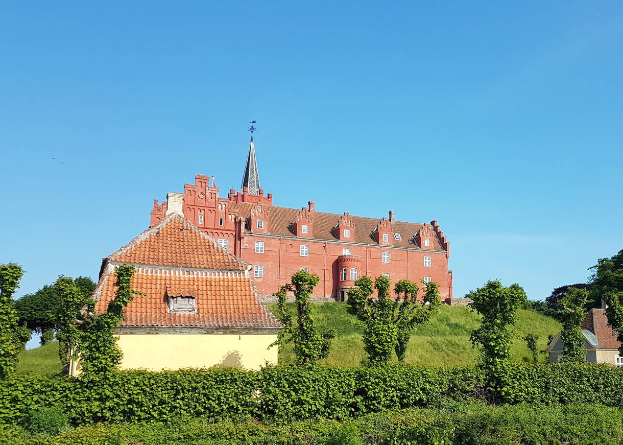 Ein rot gestrichenes Schloss auf einem Hügel hinter einem gelben Haus