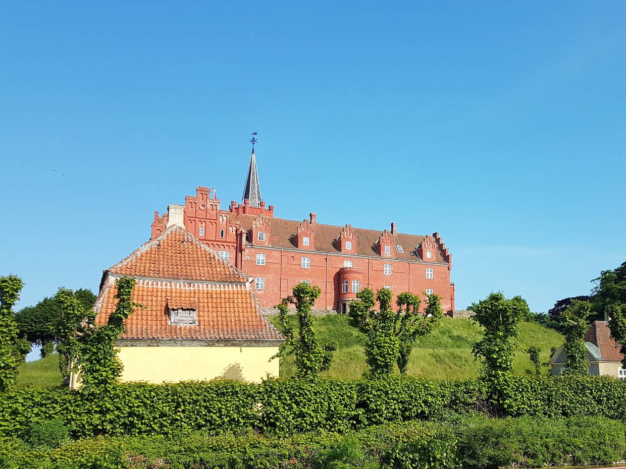 Ein rot gestrichenes Schloss auf einem Hügel hinter einem gelben Haus