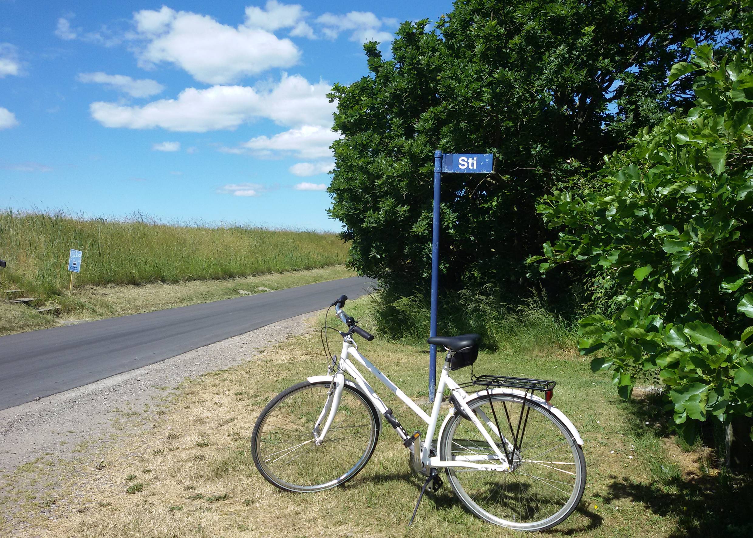 weißes Fahrrad an einem Schild vor einem Deich