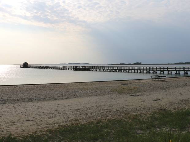Die Sonne geht unter über einen langen Holzsteg der ins Meer führt