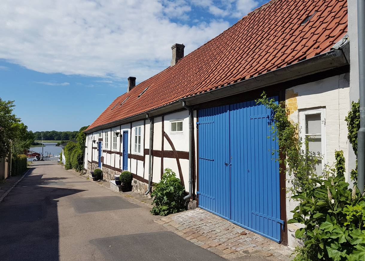 Schmale, abfallende Gasse mit einem weißen Fachwerkhaus mit blauem Tor