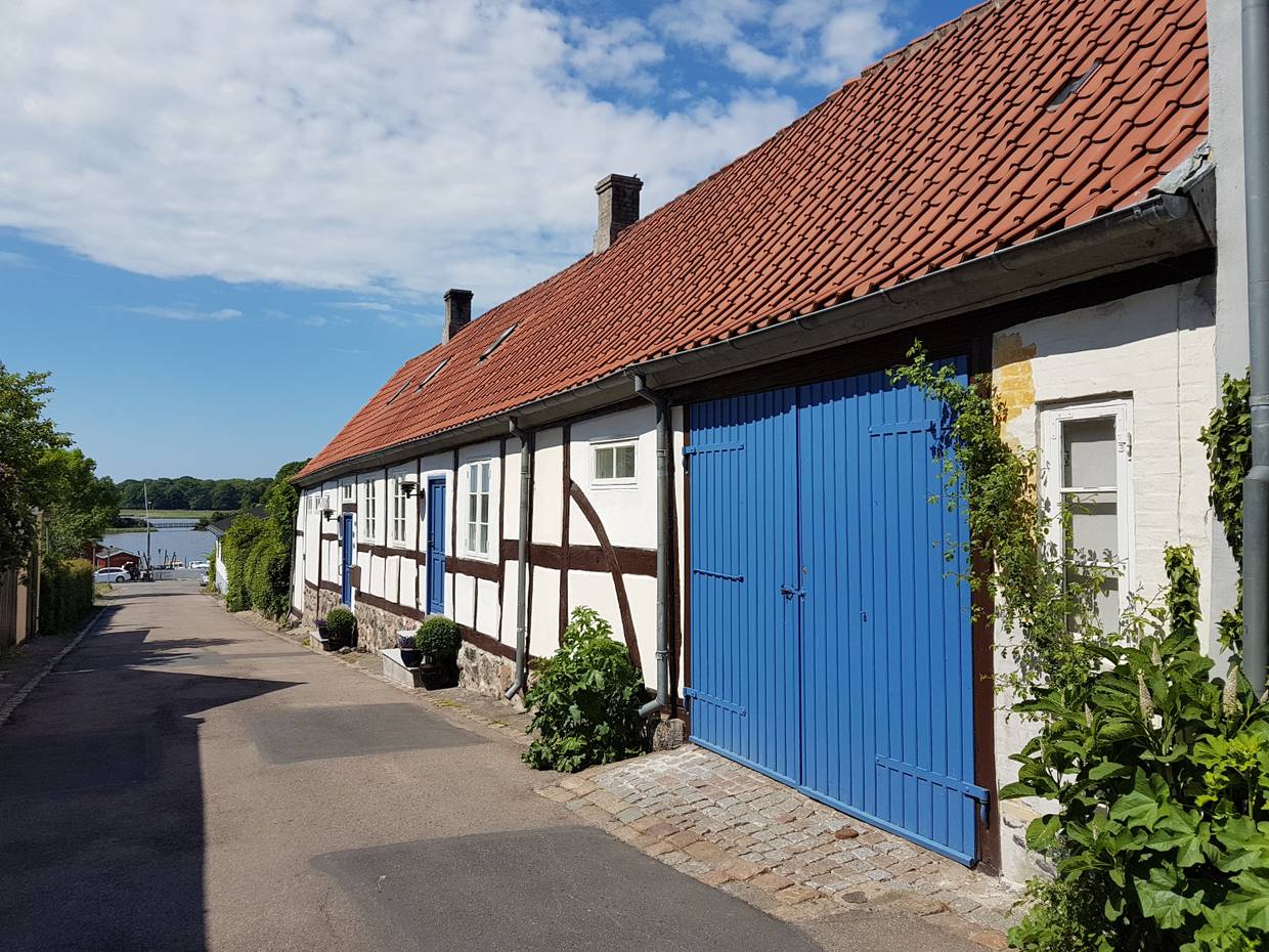 Schmale, abfallende Gasse mit einem weißen Fachwerkhaus mit blauem Tor