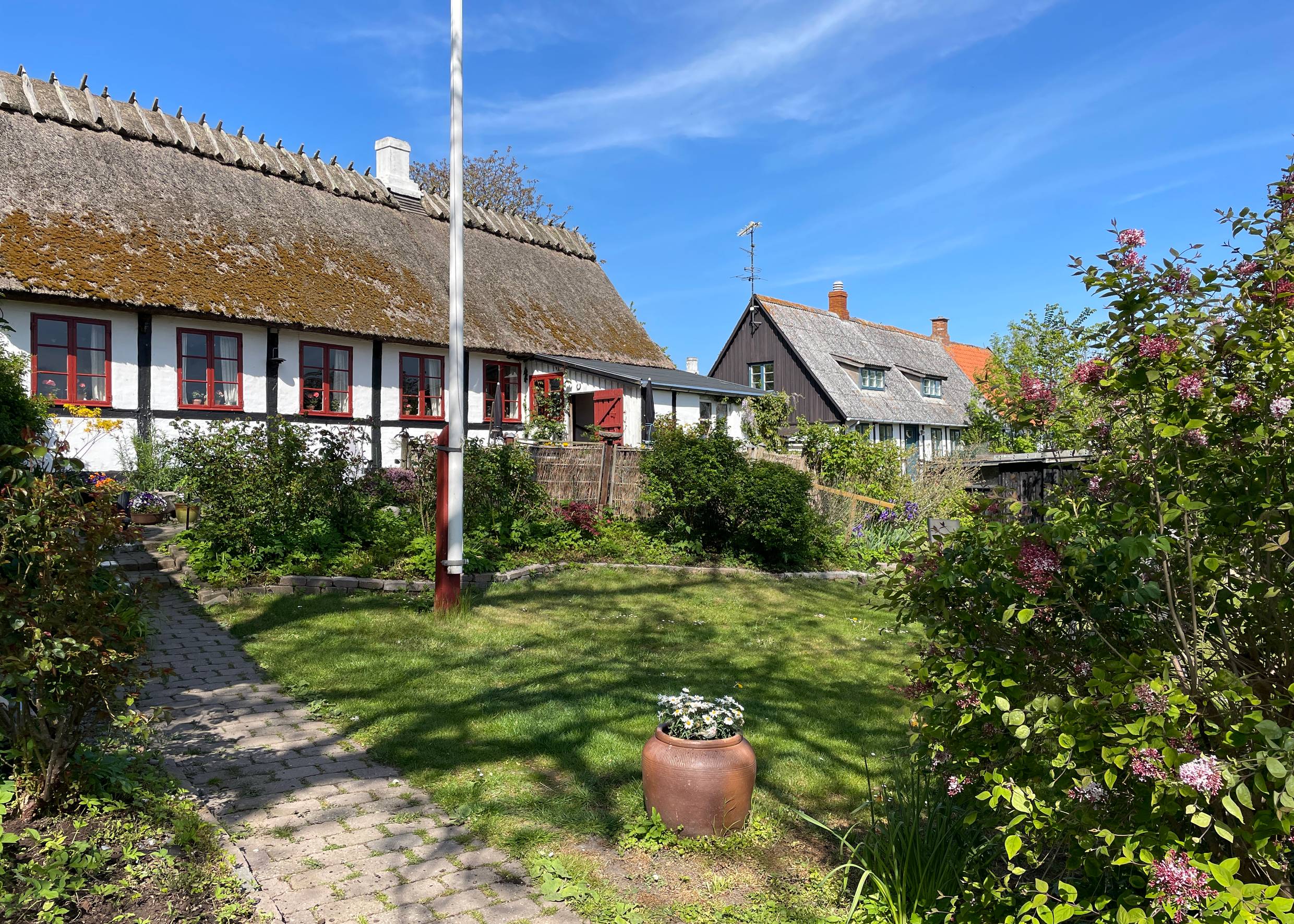 Fachwerkhaus mit Reetdach, davor ein blühender Garten mit Fahnenmast