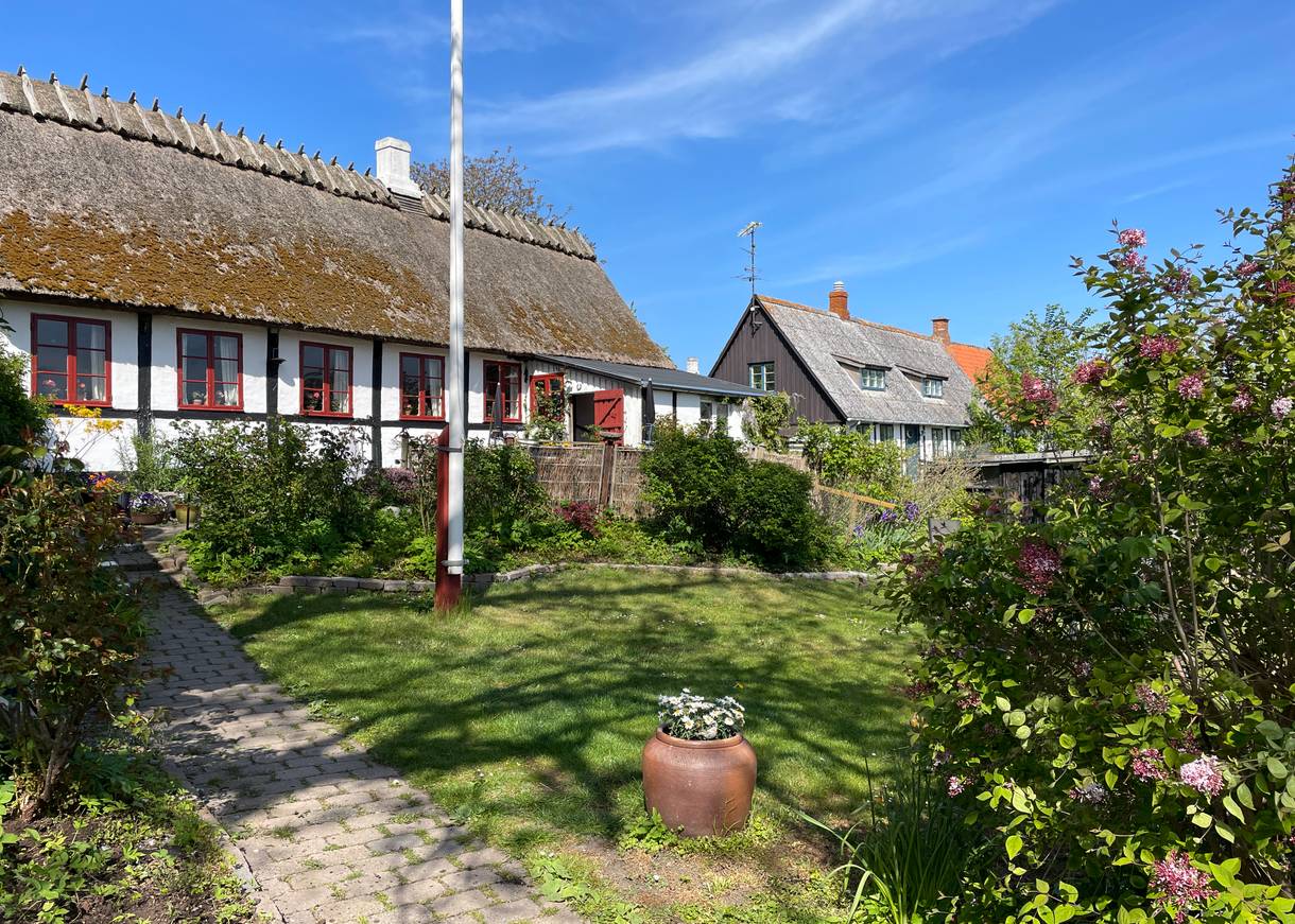 Fachwerkhaus mit Reetdach, davor ein blühender Garten mit Fahnenmast