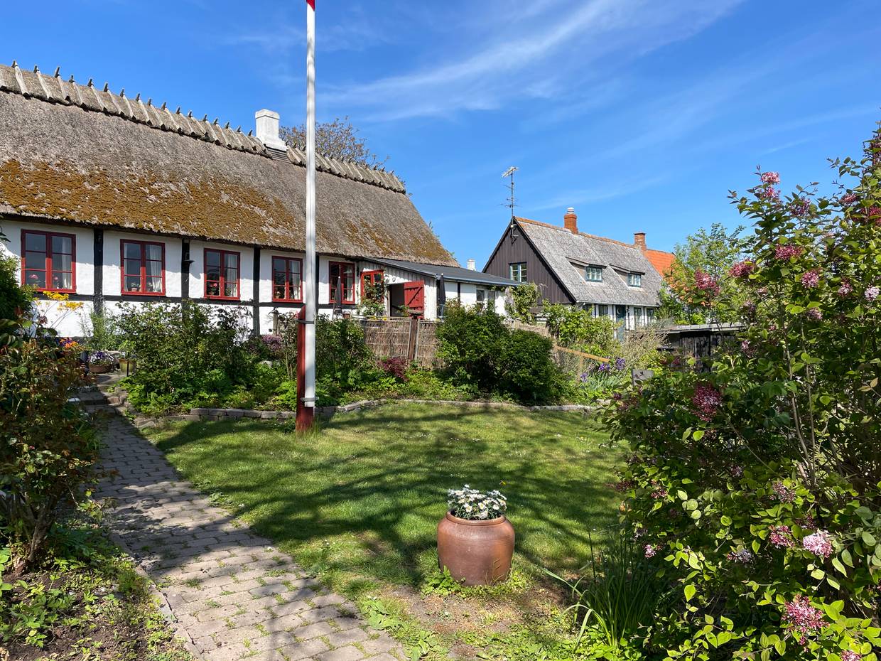 Fachwerkhaus mit Reetdach, davor ein blühender Garten mit Fahnenmast