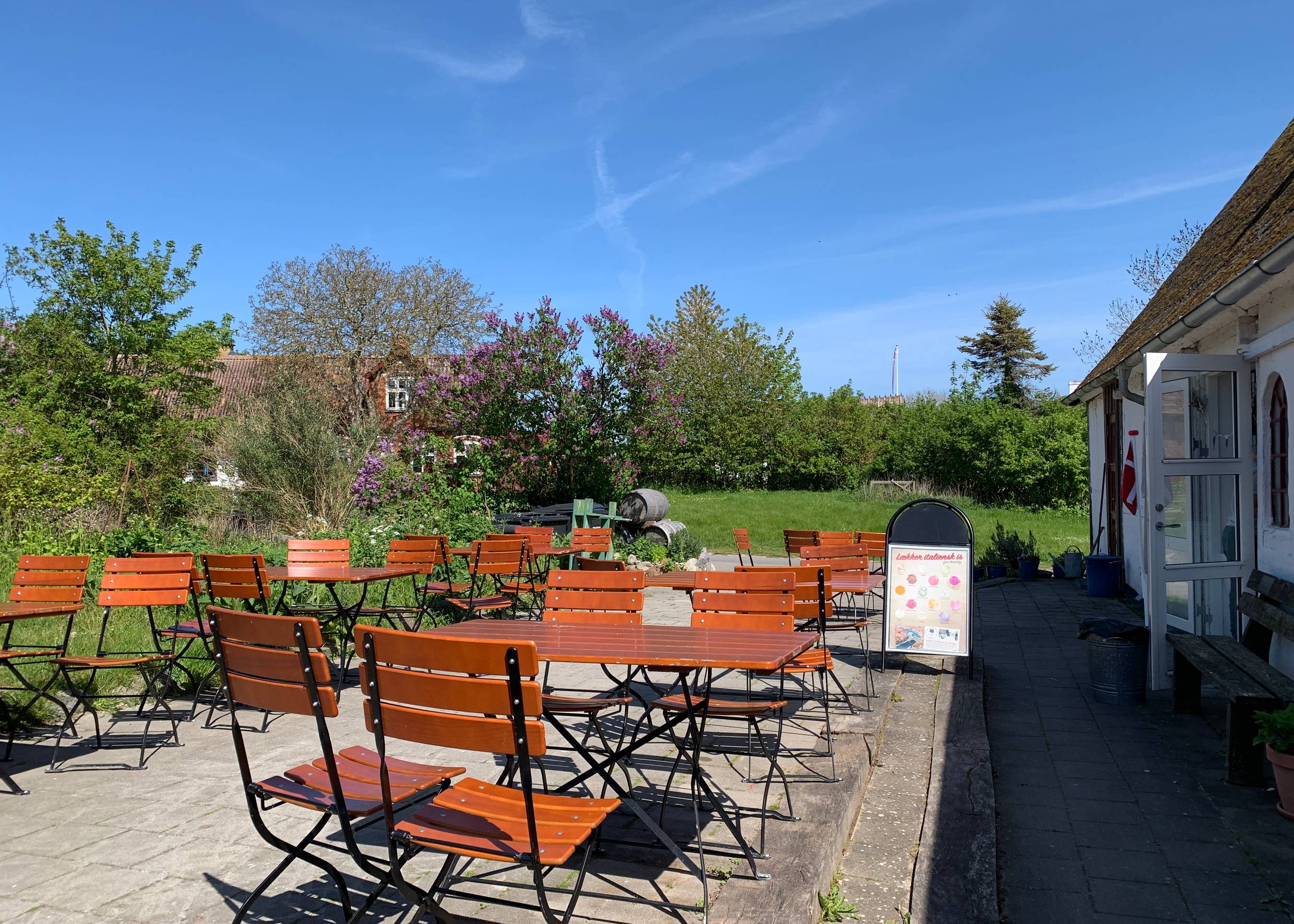 Terrasse mit vielen Sitzplätzen, dahinter ein blühender Garten