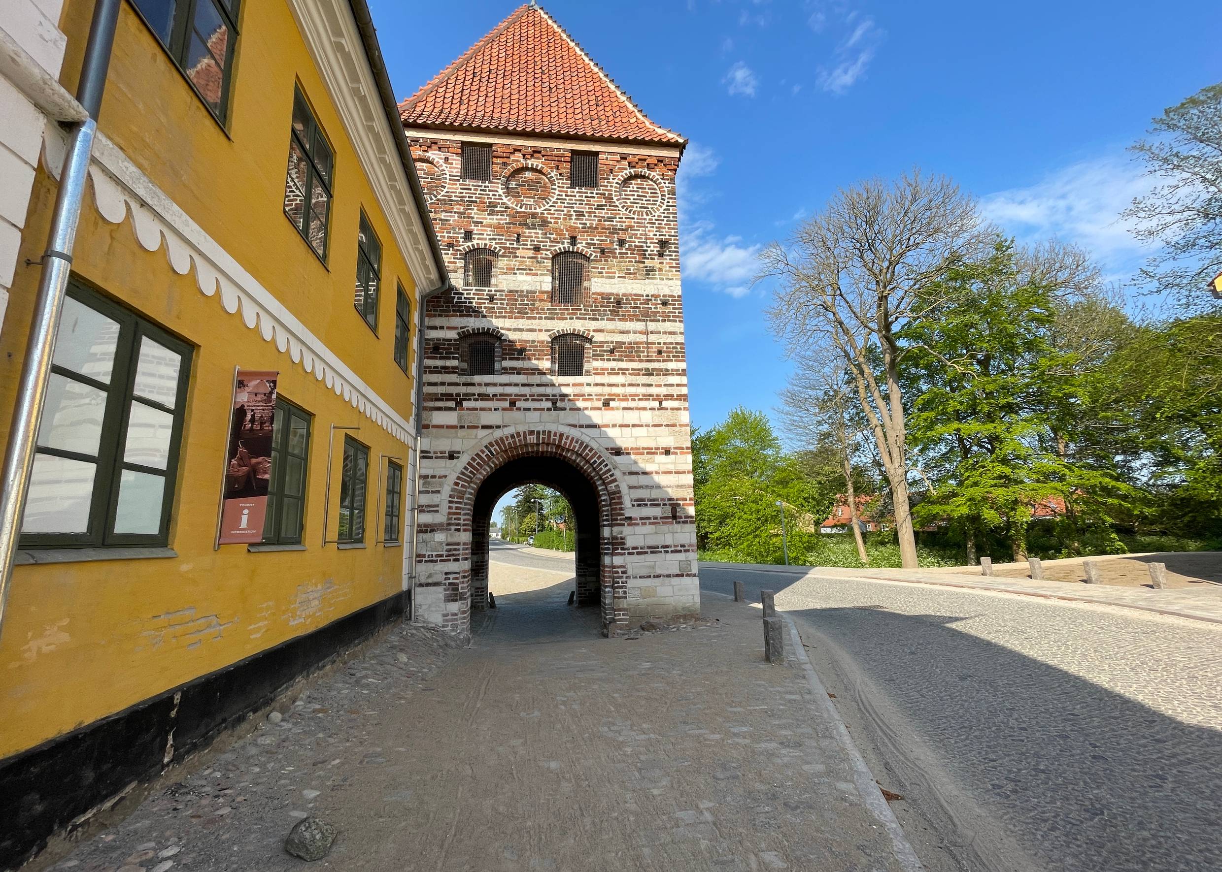 Altes Stadttor in einem Turm, der an ein gelbes, historisches Stadthaus grenzt