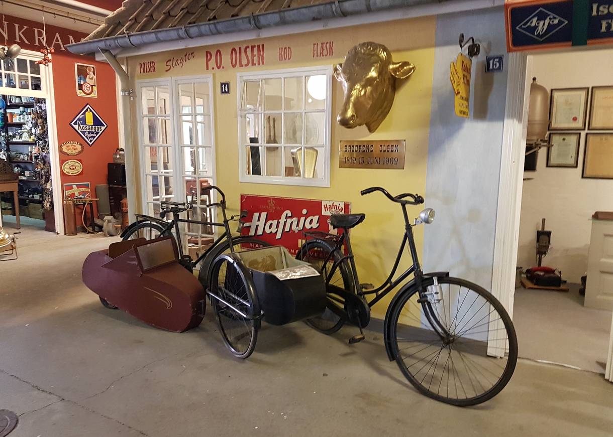 Helle Museumsräume mit einem alten Fahrrad, dahinter ein Kramerladen