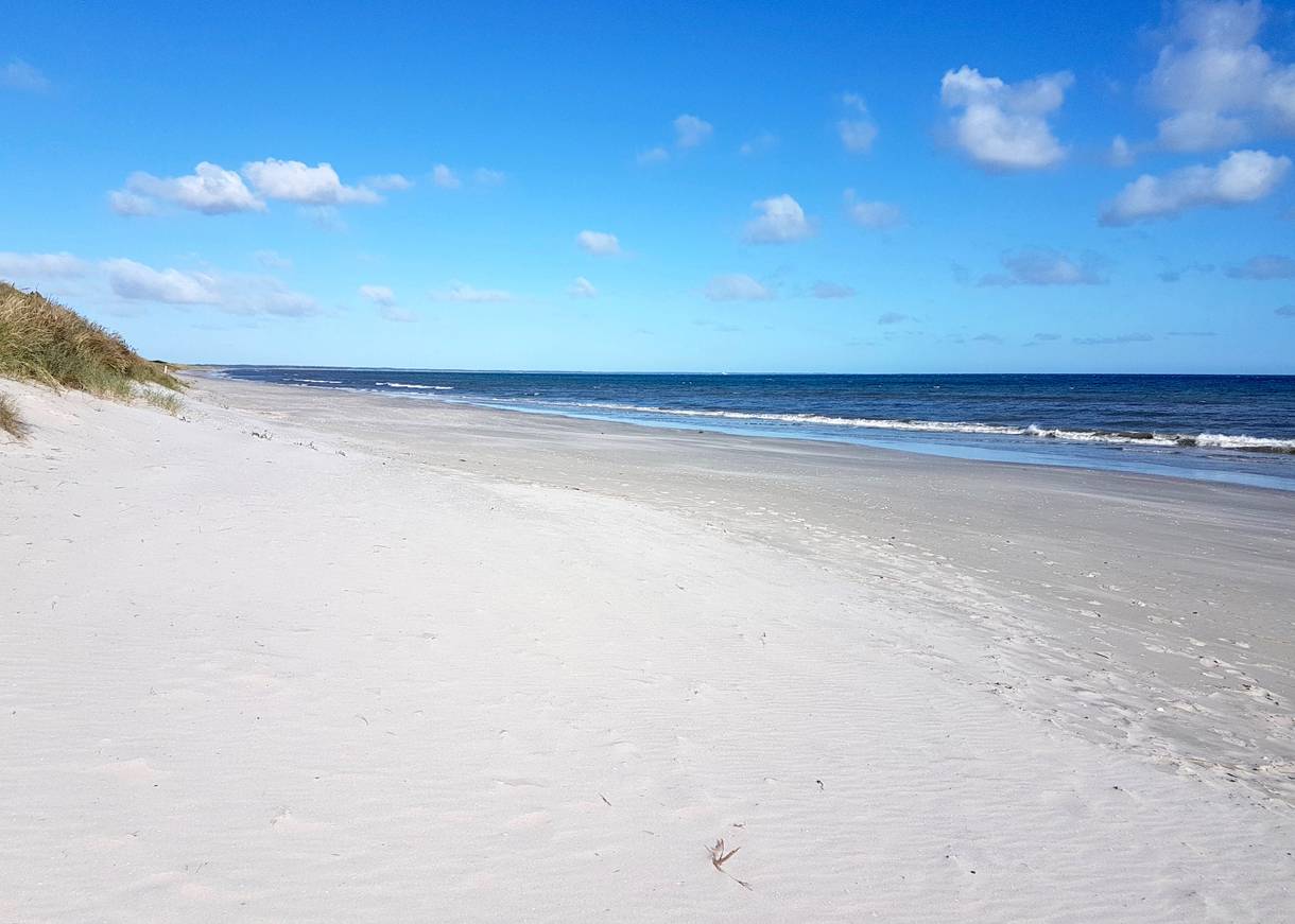 Langer, weißer Sandstrand vor einer flachen Düne
