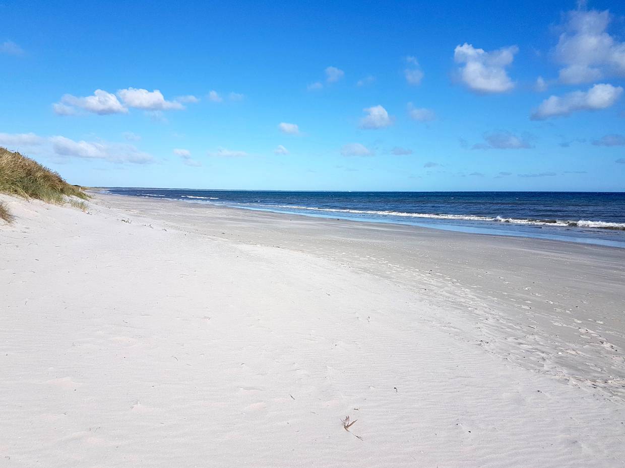 Langer, weißer Sandstrand vor einer flachen Düne