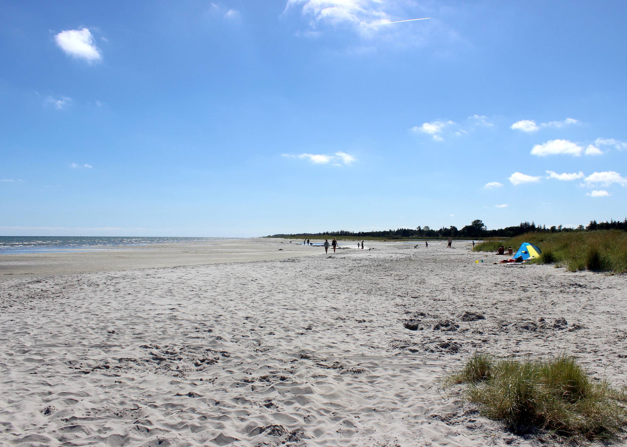 Breiter Ostseestrand mit flachem Wasser und einigen Besuchern in der Ferne