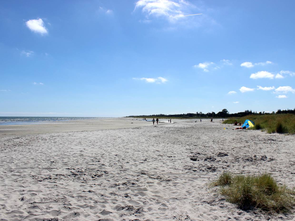 Breiter Ostseestrand mit flachem Wasser und einigen Besuchern in der Ferne