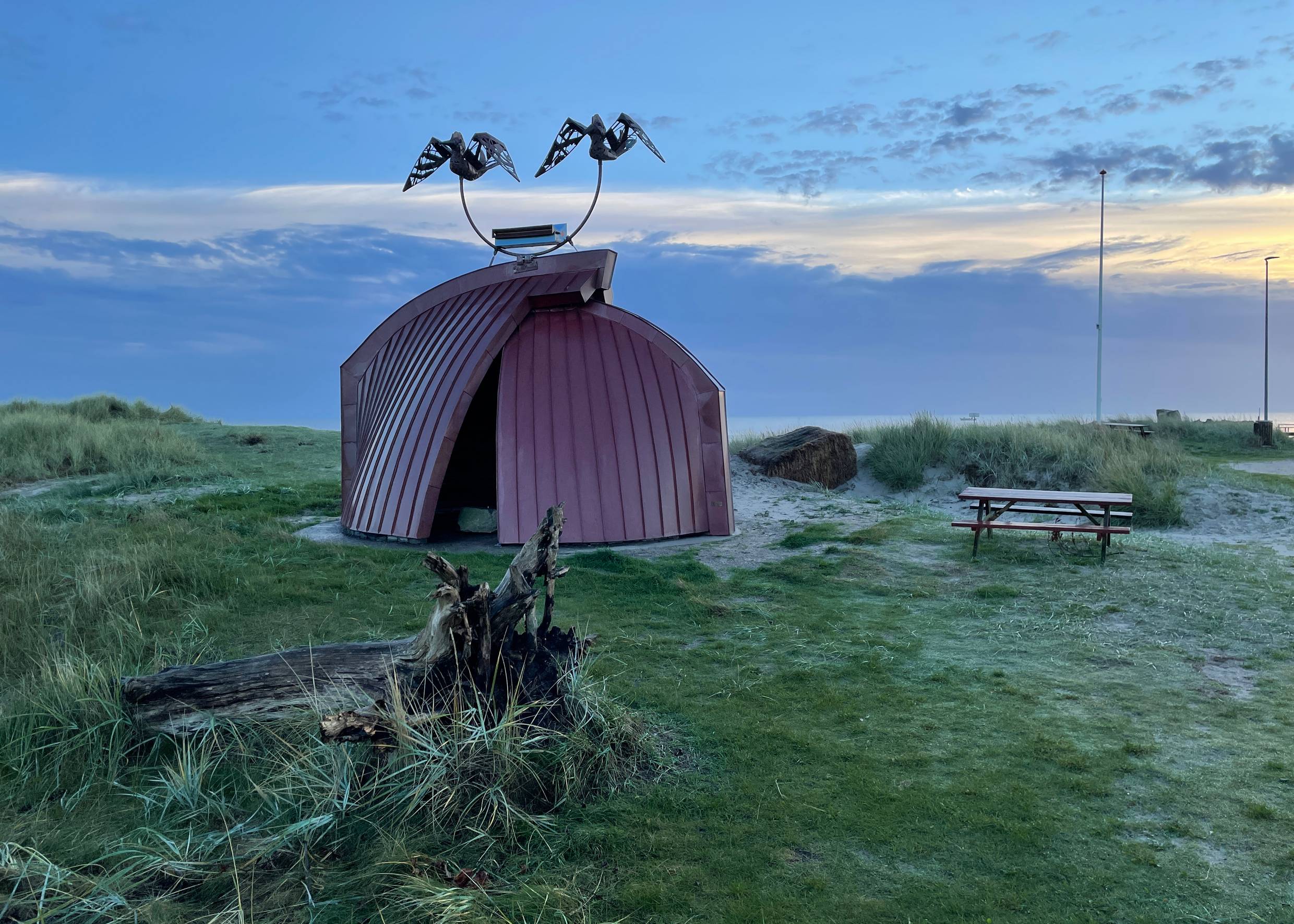 Skulptur aus zwei Bootshälften am Hafen Hou in der Abendsonne am Meer