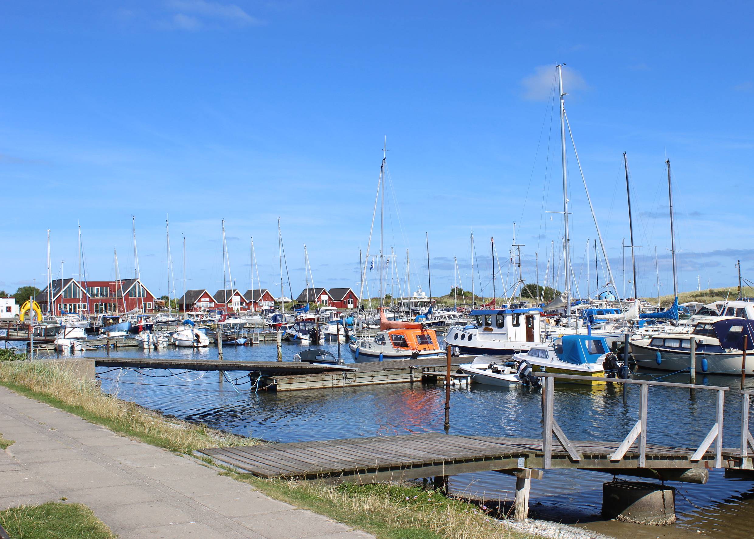 Segeljachten am Steg, dahinter rote Holzhäuser