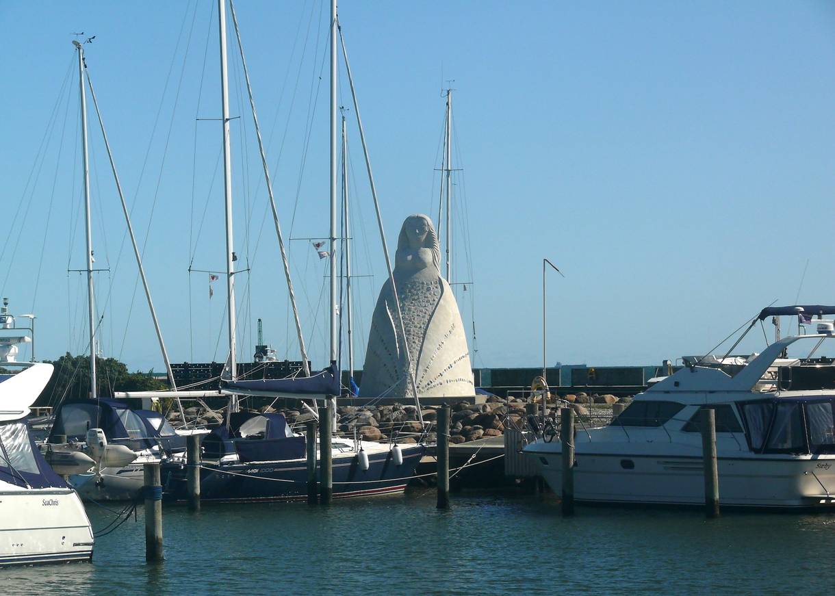 Weiße Skulptur am Hafen zwischen den Masten der Segelboote