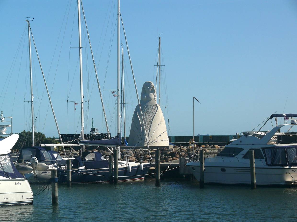 Weiße Skulptur am Hafen zwischen den Masten der Segelboote