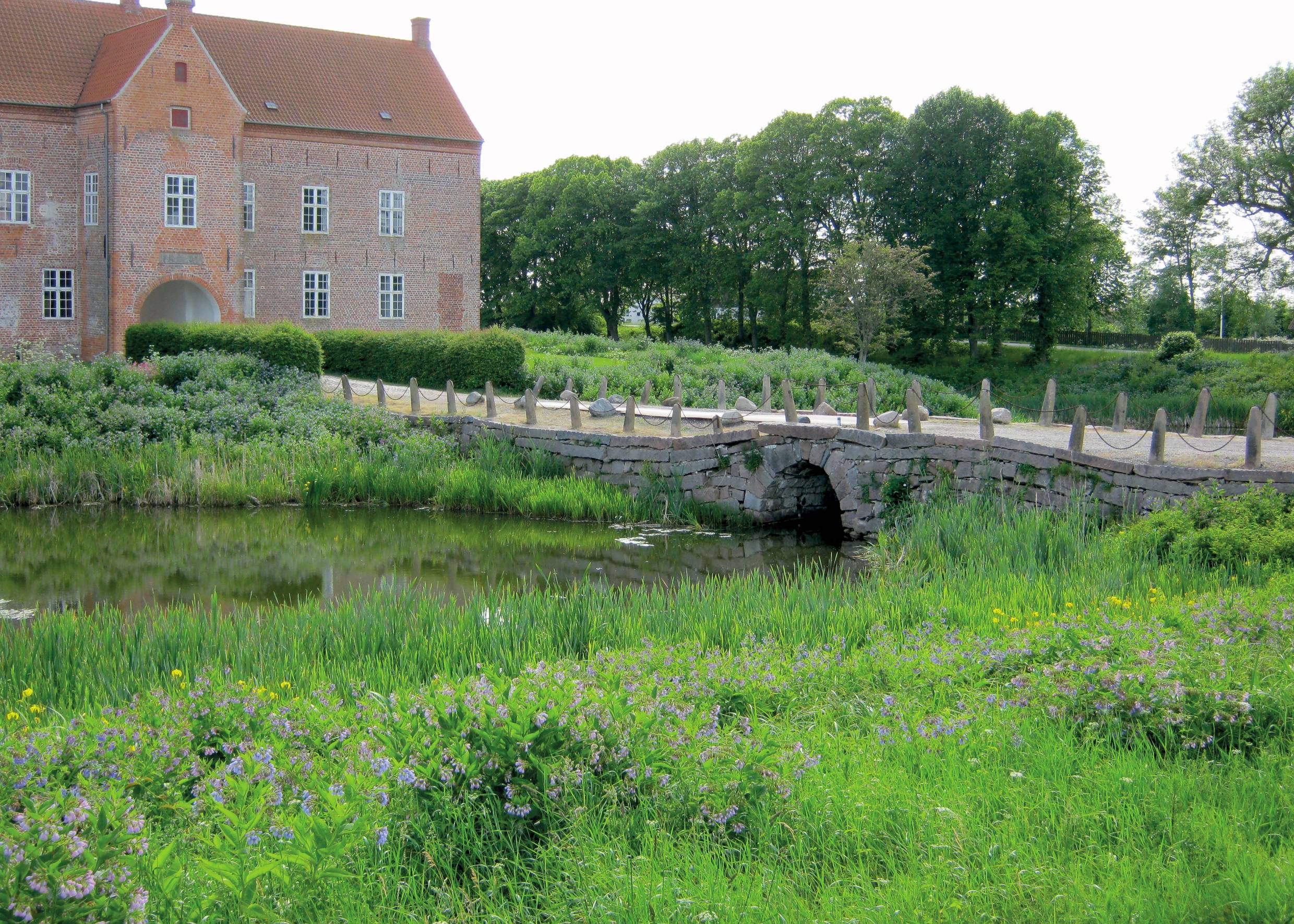 Herrenhaus aus rotem Bachstein, umgeben von einem Graben mit einer flachen Brücke