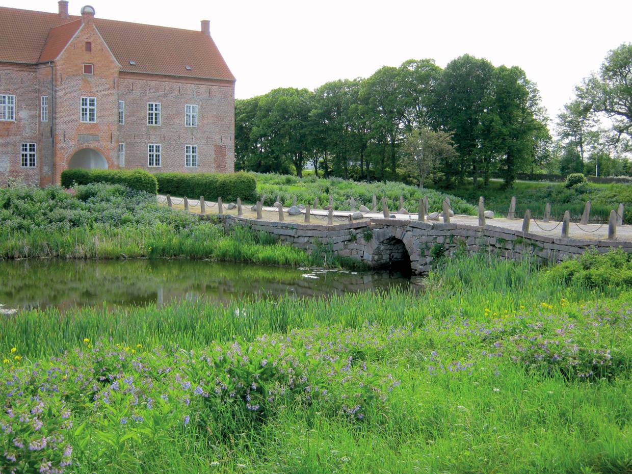 Herrenhaus aus rotem Bachstein, umgeben von einem Graben mit einer flachen Brücke
