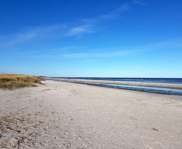 Breiter und flacher Sandstrand in einer Bucht, im Hintergrund sind Gebäude zu erkennen
