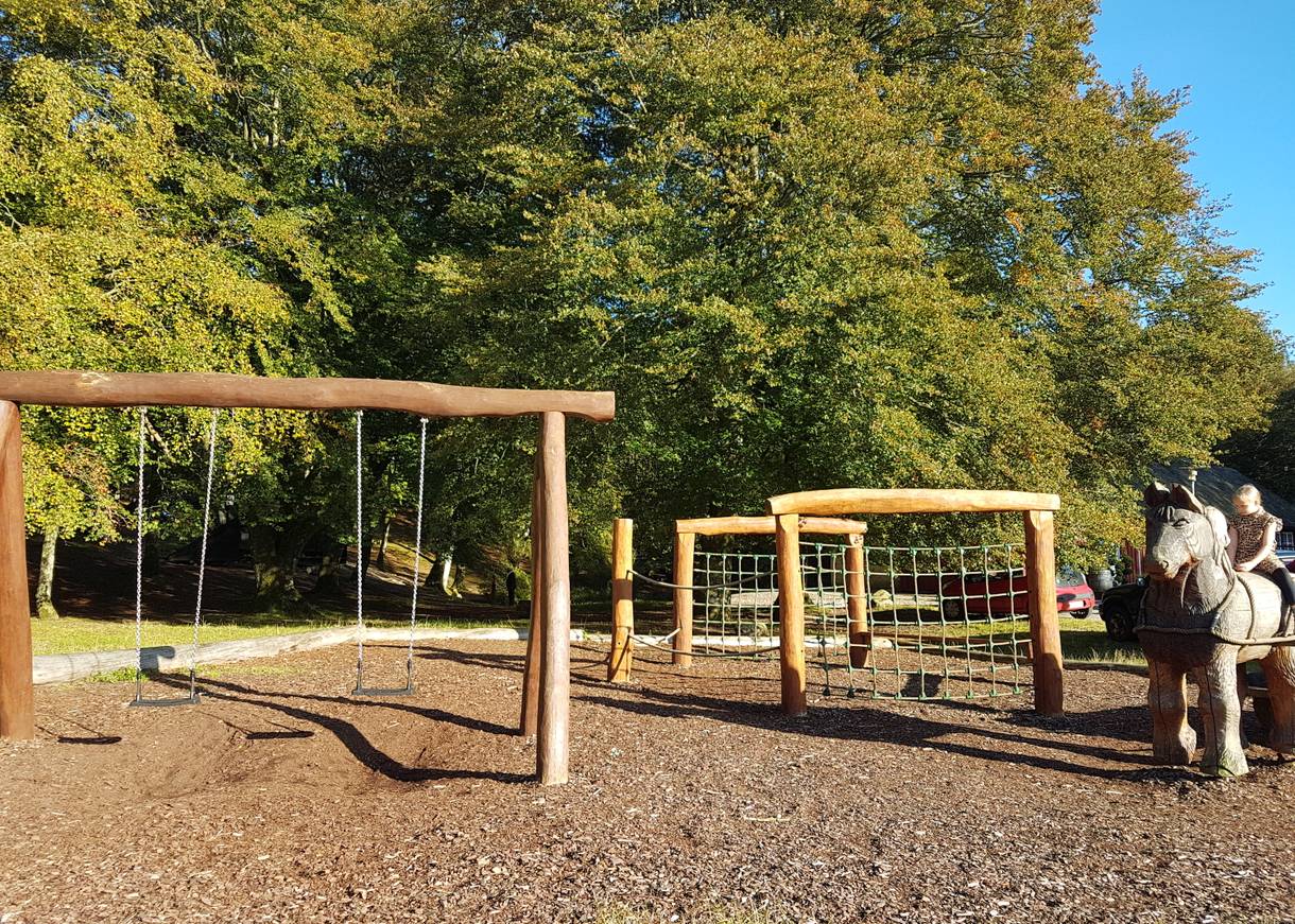 Spielplatz unter bunten Laubbäumen, rechts ein Kind auf einem Holzpferd
