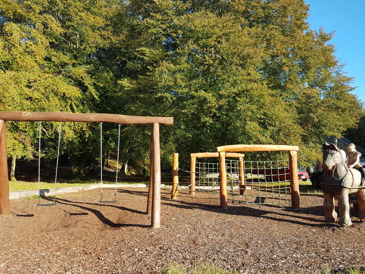 Spielplatz unter bunten Laubbäumen, rechts ein Kind auf einem Holzpferd