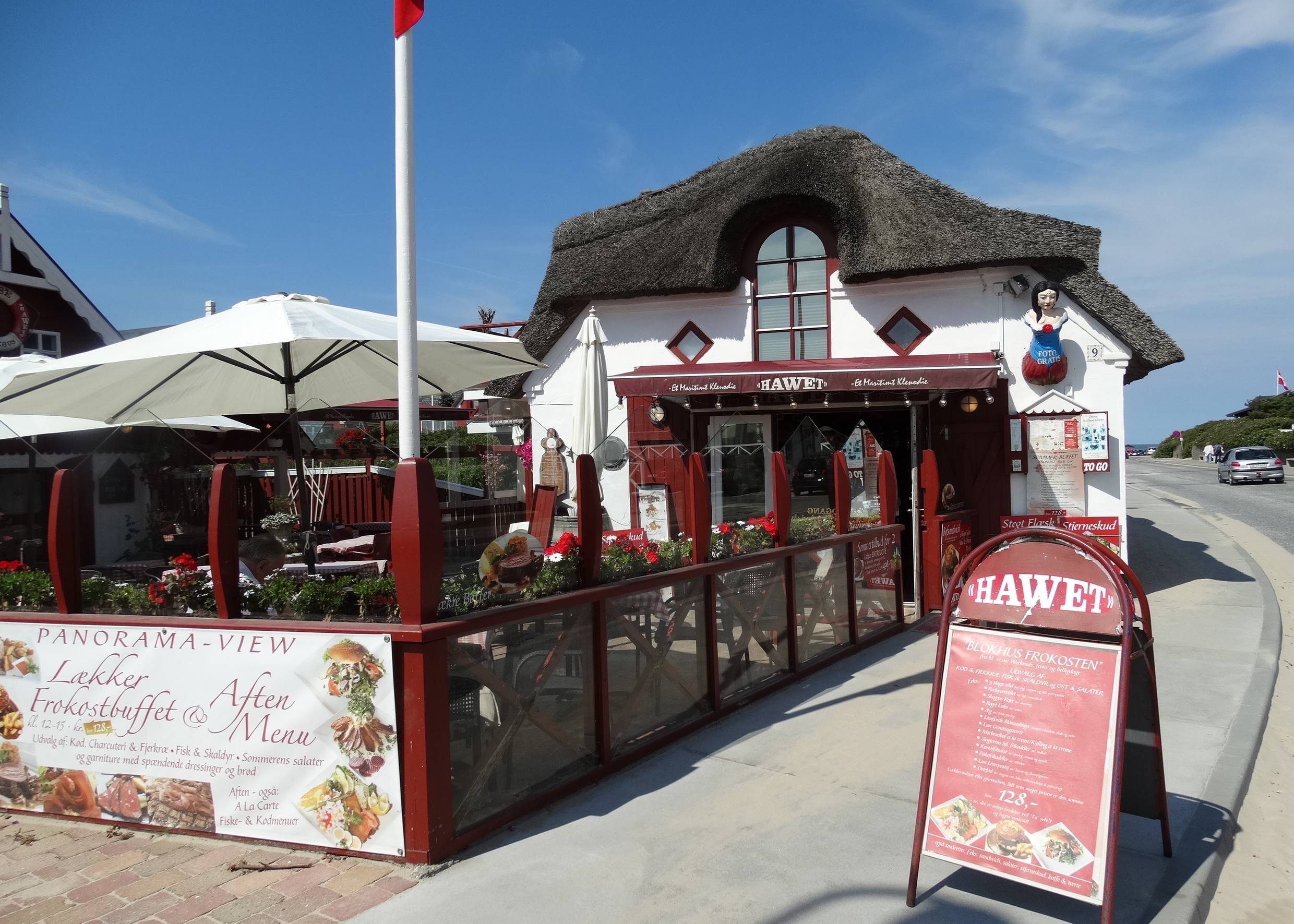 Weißes Restaurant mit Reetdach und Gastterrasse mit Windschutz