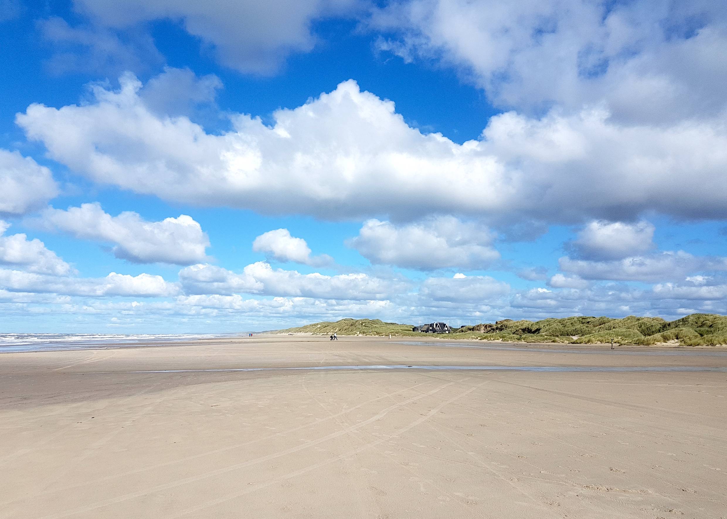Sehr breiter Strand, im Hintergrund ein Haus an den Dünen