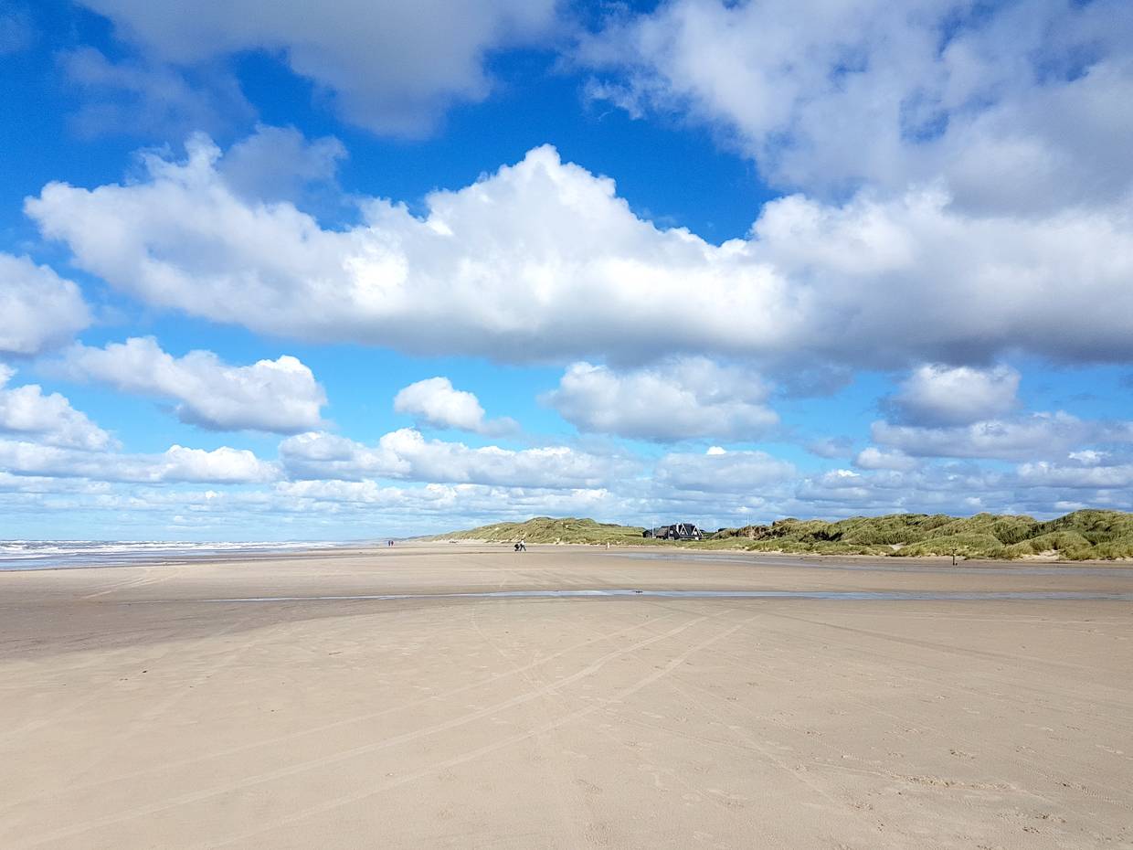 Sehr breiter Strand, im Hintergrund ein Haus an den Dünen