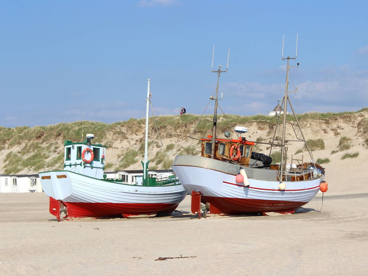 Zwei Fischerboote auf dem Strand mit Dünen im Hintergrund