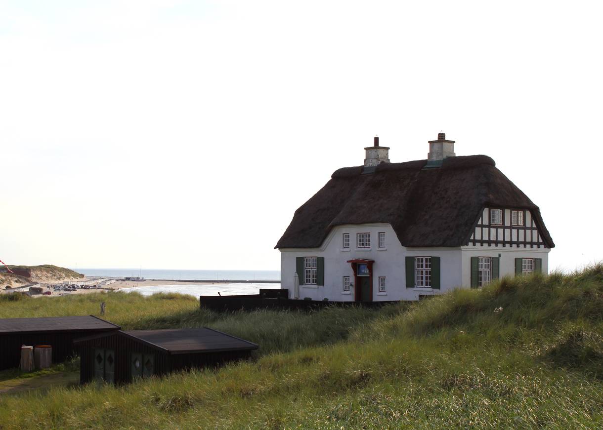 Großes, weißes Reetdachaus auf einer Düne am Meer