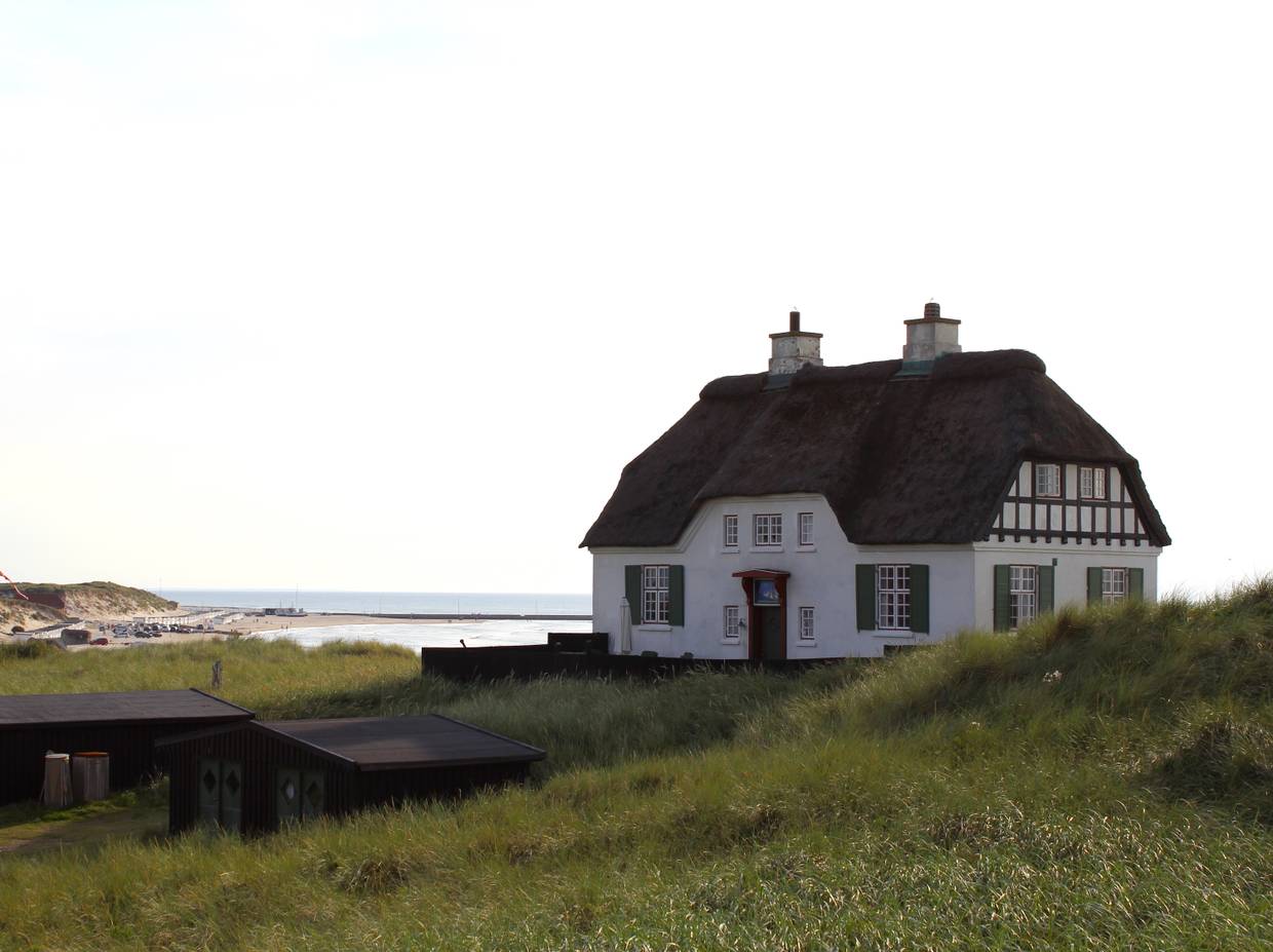 Großes, weißes Reetdachaus auf einer Düne am Meer