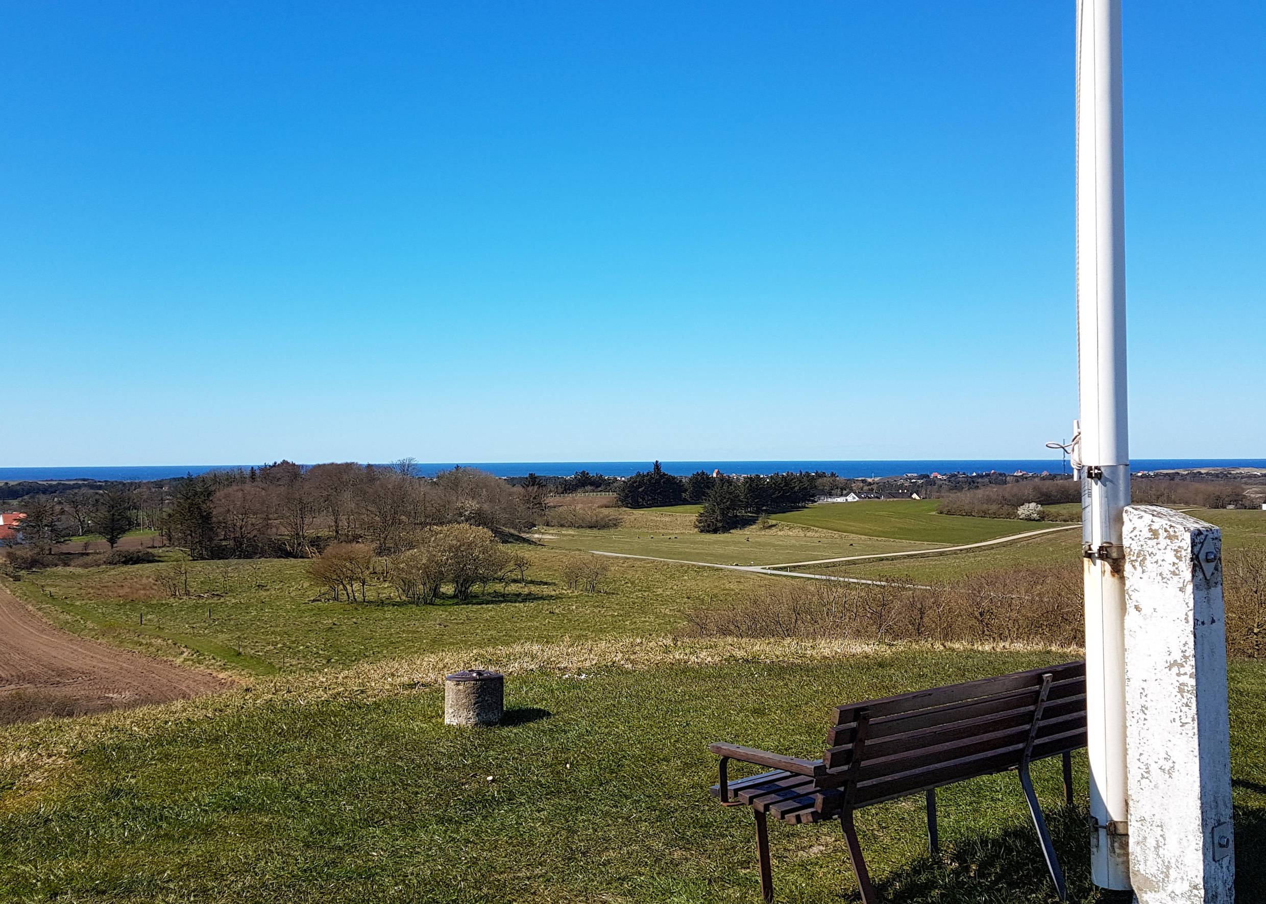 Bank neben einem Fahnenmast mit Blick über die Landschaft zur Nordsee