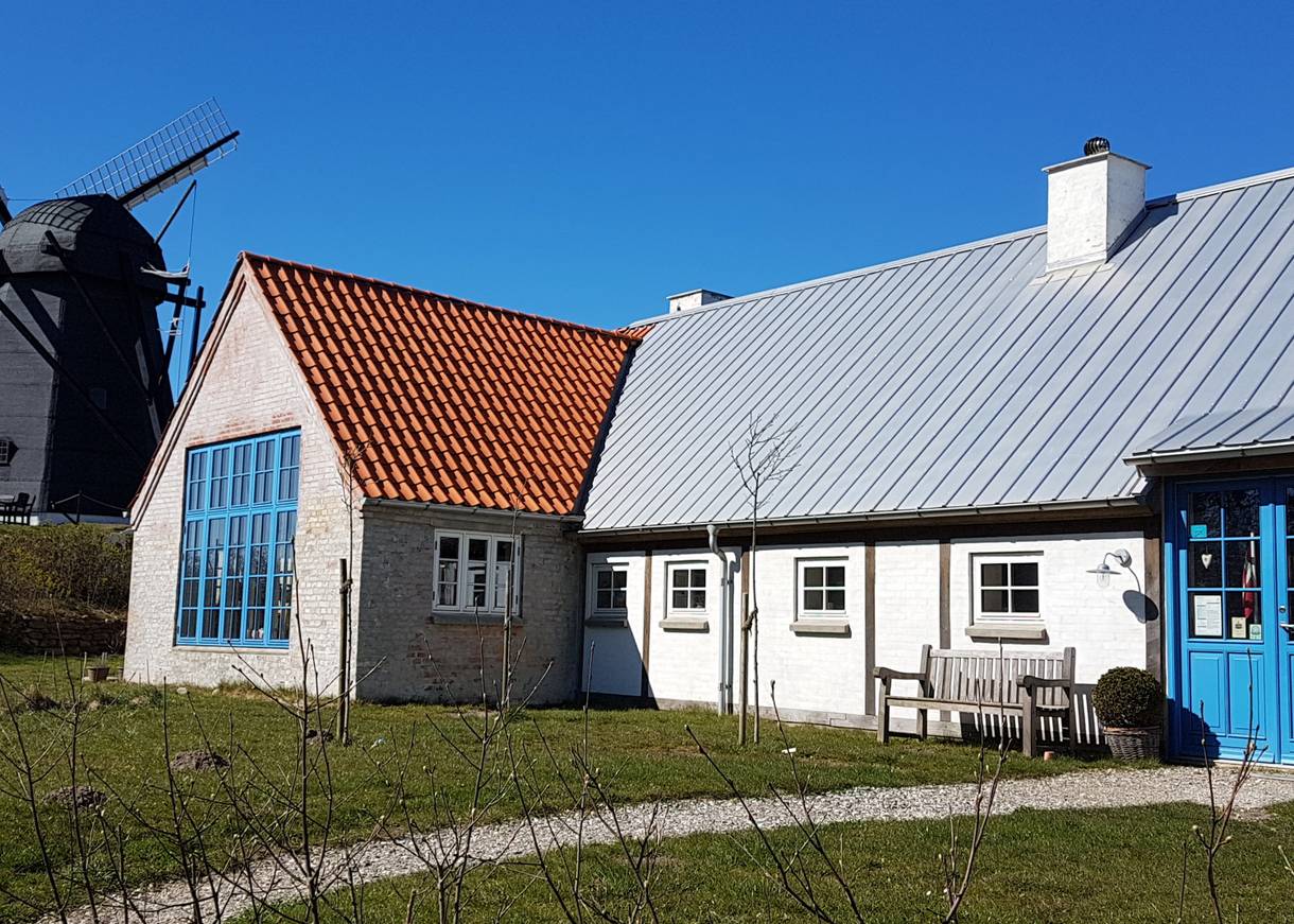 Weißer Hof mit himmelblauen Türen, dahinter eine Windmühle