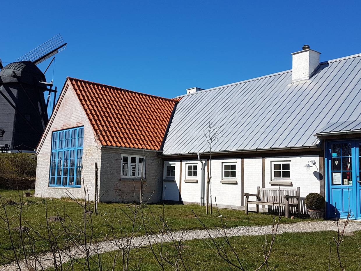 Weißer Hof mit himmelblauen Türen, dahinter eine Windmühle