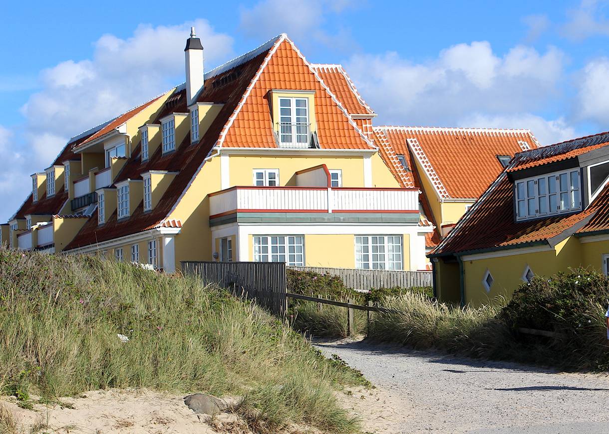 Gelbes, mehrstöckiges Ferienhaus in Skagen neben einer Düne