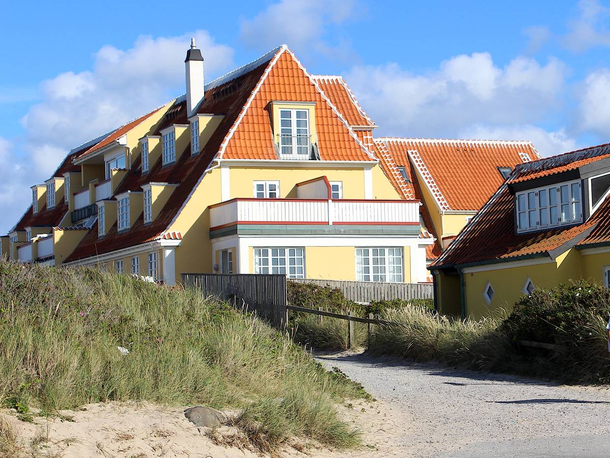 Gelbes, mehrstöckiges Ferienhaus in Skagen neben einer Düne