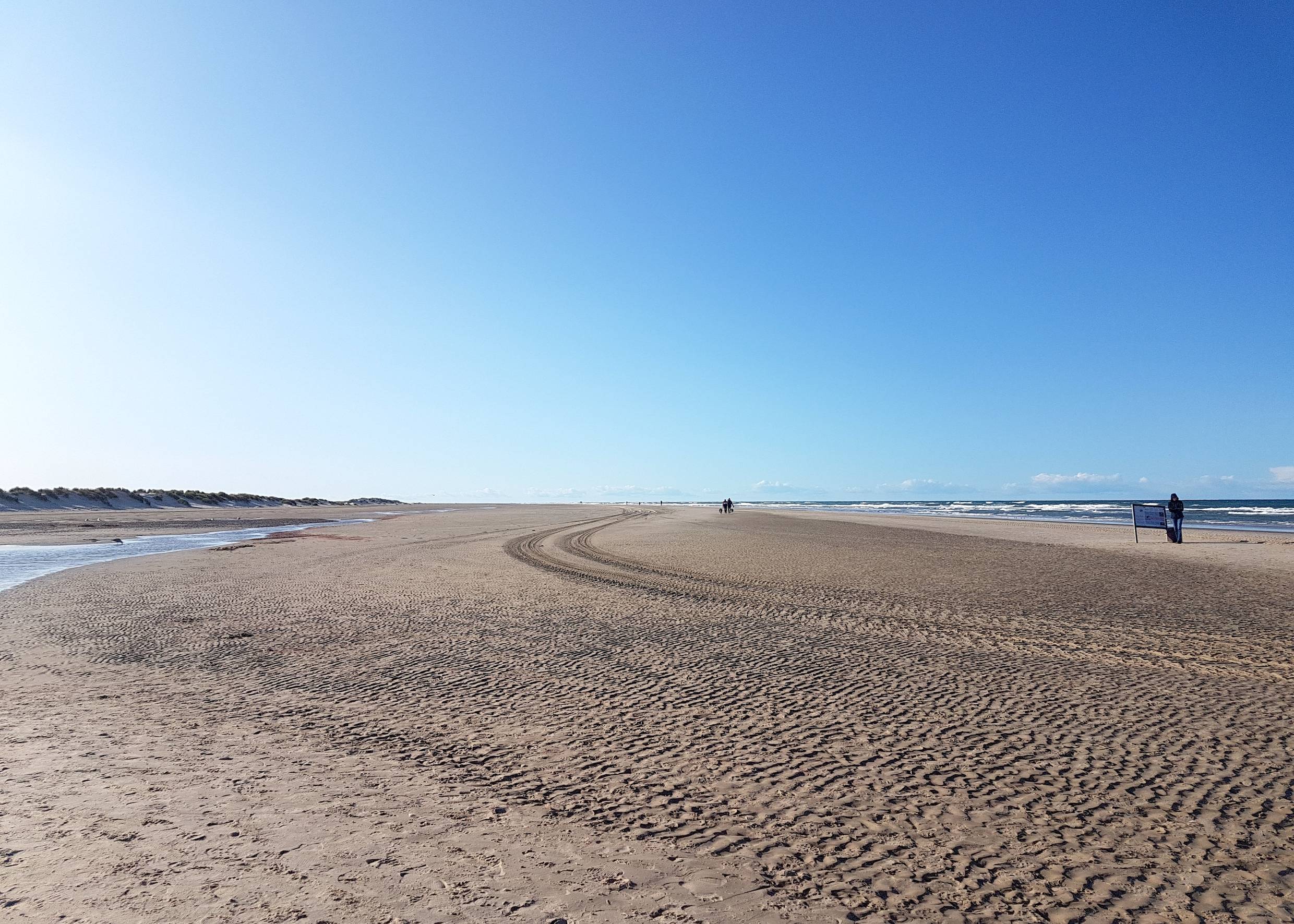 Breiter Strand mit Treckerspuren und vereinzelten Spaziergängern